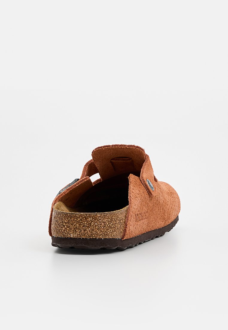 Braune Wildleder-Pantoletten mit offenem Rücken, Korksohle und verstellbarem Riemen, von hinten auf weißem Hintergrund gezeigt.
