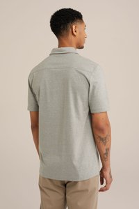 Polo triko s krátkým rukávem, světle šedé barvy, s límečkem, slim fit střih, jednoduché švy, doplněné béžovými kalhotami.