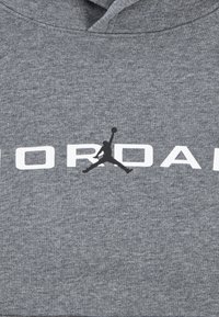Sweat à capuche gris avec un tissu texturé. Présente un grand texte "JORDAN" en blanc et un logo en silhouette noire d'une figure sautant au centre.