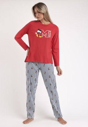 Mujer con camiseta roja de manga larga con gráfico de Mickey Mouse y pantalones blancos a rayas con pequeños dibujos de Mickey Mouse, de pie descalza.