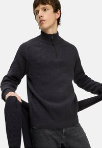 Dunkelgrauer Strickpullover mit hohem Kragen und Reißverschluss. Besitzt ein strukturiertes, geripptes Muster und lange Ärmel. Stilvolles und zugleich funktionales Design.