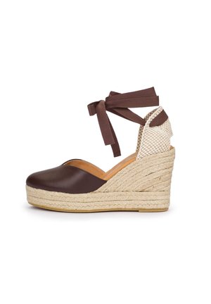 Brown closed-toe wedge shoe with braided jute platform, cream woven heel counter, and brown fabric ankle ties.