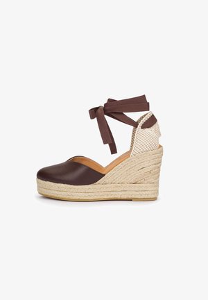 Zapato cuña cerrado marrón con plataforma de yute trenzado, contrafuerte de talón tejido en crema y cordones marrones de tela para el tobillo.