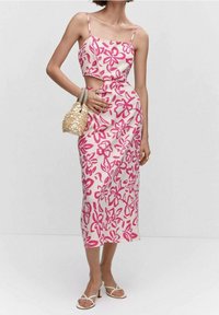 Różowa sukienka w kwiatowy wzór składająca się z dwóch części, z ramiączkami spaghetti i dopasowaną talią. Modelka trzyma torebkę z koralikami, w połączeniu z sandałami na obcasie.