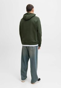 Olivenfarvet hættejakke med snor i hætten, parret med løstsiddende lyseblå denimjeans og sorte sneakers med hvide såler.
