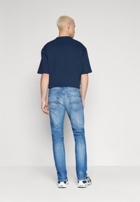 Camiseta de algodón azul marino de mangas cortas, combinada con jeans de color azul claro. Modelo lleva zapatillas negras y blancas con detalles en verde.