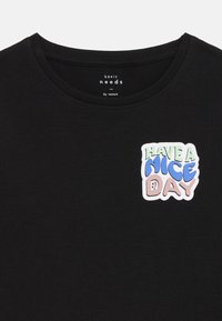 Fekete pamut póló, kerek nyakkivágással és a bal mellrészen található, színes grafikával, amely a "HAVE A NICE DAY" feliratot tartalmazza.