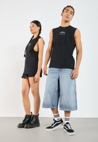Čierny bezrukávový top s logom, čierne šortky, čierne bojové topánky; rifľové culottes, čierne tričko, pruhované ponožky, čierne tenisky.