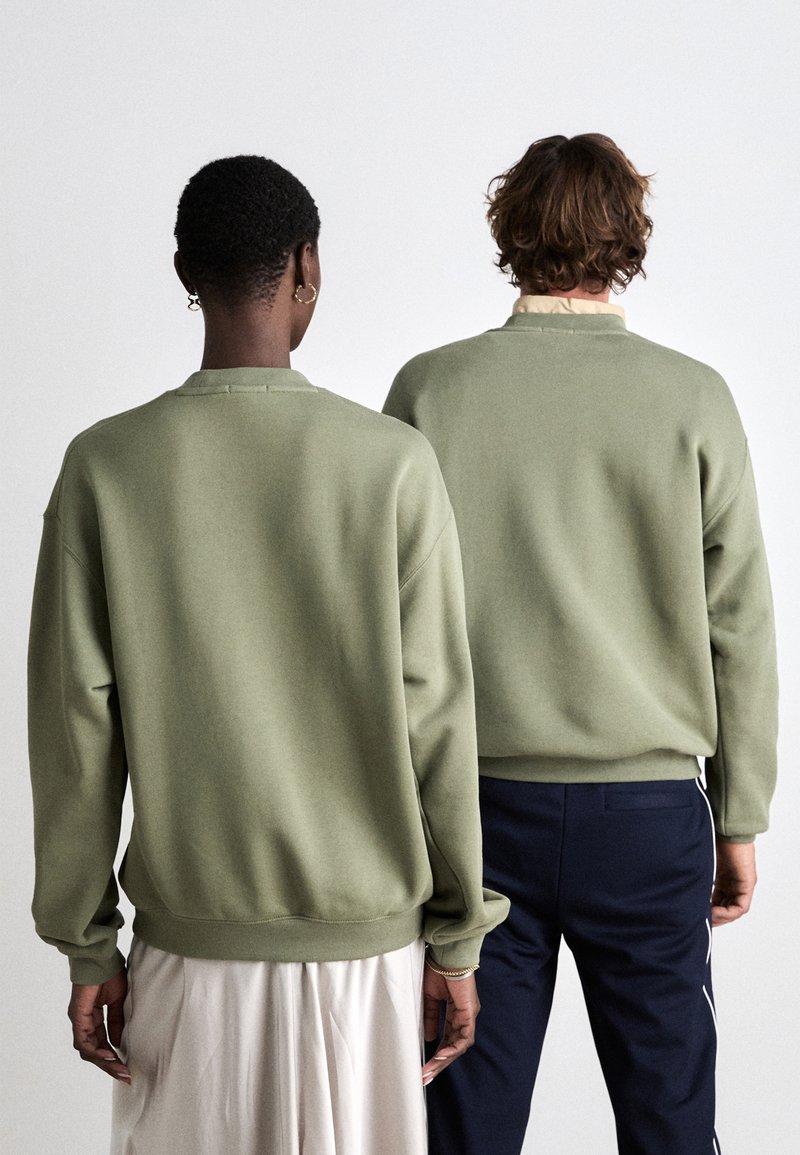 Felpe verde oliva con colletto rotondo e orli a coste, indossate da due persone. Una ha le maniche lunghe; l'altra è sovrapposta a una camicia con colletto.