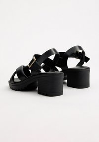 Las sandalias de tacón negro cuentan con amplias correas de cuero, una suela gruesa y texturizada, y una hebilla ajustable en la correa del tobillo para un ajuste seguro.