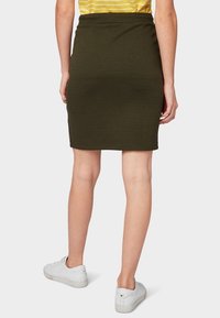 Zelenohnědá přiléhavá sukně vyrobená z elastického materiálu, s délkou do poloviny stehen a hladkou texturou, doplněná bílými teniskami.