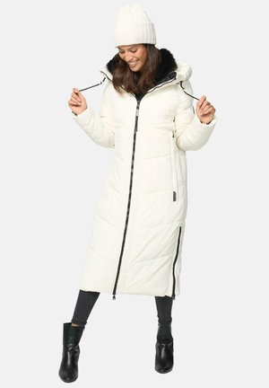 Manteau long en duvet blanc avec une fermeture éclair noire, capuche en fourrure et poches latérales. Porté avec un bonnet en tricot crème et des bottes noires à la cheville.