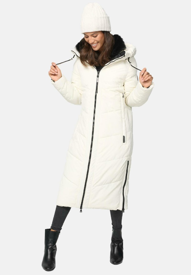 Balta gara pūkaina lietussarga coat ar melnu rāvējslēdzēju, kažokādas oderi kapuci un sānu kabatām. Valkāta ar krēmīgu adīto beanie un melnām potīšu zābakiem.
