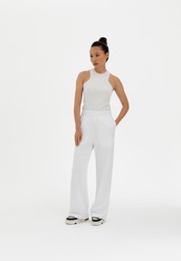 White ribbed tank top paired with loose white sweatpants. The outfit features a relaxed fit and is complemented by black and cream sneakers.