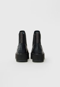 Pair of black ankle boots with platform heels, ribbed fabric uppers, and a zigzag pattern on the back pull tabs, shown from the rear.