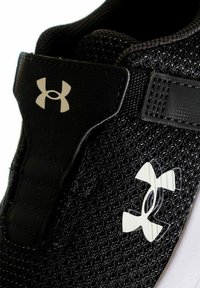 Scarpa da ginnastica nera con tomaia in mesh testurizzato e accenti neri lisci. Presenta un logo bianco e una fascia regolabile per una vestibilità sicura.