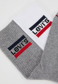 Socken aus grauem und weißem Strick mit gerippter Textur. Jede Socke hat ein Logodesign mit navyblauen und roten Akzenten für den Kontrast.