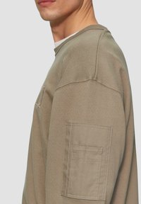 Beige sweatshirt van textiel met een gestructureerde stof, ronde hals en een patchzak op de linkermouw; minimalistisch ontwerp met strakke lijnen.
