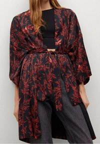 Kimono floral noir et rouge avec un design ample, tissu fluide et manches larges, noué à la taille. Associé à un haut noir et un jean foncé.