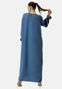 Lang, løstsiddende blå kjole lavet af glat stof, med klokkeærmer, nøglehul i ryggen og en lige silhuet.