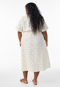 Vestido de longitud hasta el tobillo con estampado floral en tela color crema con textura acanalada. Mangas cortas, cintura elástica y corte holgado. Sandalias marrones visibles.