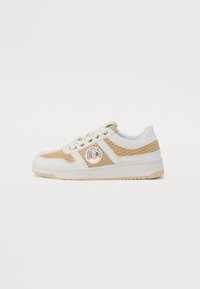 Hvite og beige sneakers med teksturerte mesh-paneler, avrundet tå og en fremtredende logo-patch. Flat gummisåle med subtilt mønster.
