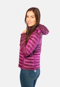 Doudoune violette avec capuche, présentant des sections matelassées et une texture lisse. Portée sur un denim, mettant en avant un design ajusté.