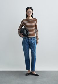 Brown and white striped long-sleeve top, blue jeans, and black flats. Black bag in hand. Simple design, fitted style, and casual look.