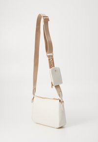 Biała torebka crossbody o teksturowanej powierzchni z złotym zamkiem, beżowym paskiem i odpinaną dopasowaną mini saszetką. Zawiera subtelne, wytłoczone wzory.