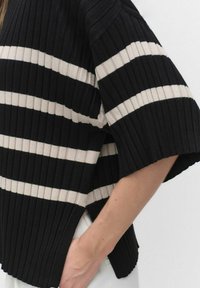 Oversized gestreepte trui in zwart en crème met ribstructuur, featuring ruime mouwen en een casual pasvorm met zijsplitten voor extra comfort.