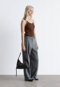 Ribbed brown tank top with front buttons, paired with grey pleated pants. Black woven handbag and black shoes, with a gold chain bracelet.