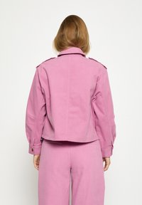 Rozā džinsa jaka ar plecu epauletēm, īss griezums un garas piedurknes, komplektā ar atbilstošām biksēm. Gluda tekstūra, minimālas šūšanas detaļas.