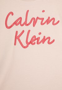 T-shirt rosa chiaro con grande scritta rossa in rilievo "Calvin Klein". Il tessuto appare liscio con un design classico a girocollo.