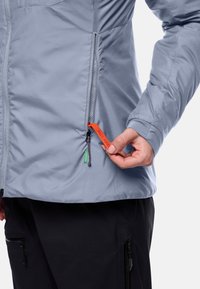 Lichtblauwe waterdichte jas met ritszakken. Bevat een oranje trekkoord met het label 'PACK AWAY' en groene accentdetails.