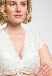 Witte kanten bralette met korte mouwen, met plooien in het midden en een golvende halslijn. Glad textuur met bloemmotieven.