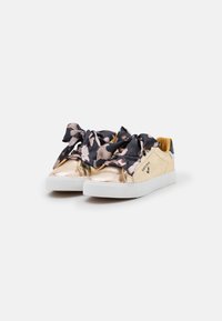 Sneaker metallizzati dorati con grandi fiocchi a motivi floreali neri e rosa; suole in gomma bianca; texture liscia; design minimalista.