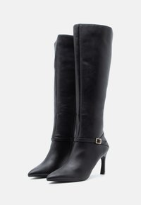 Stivali neri in pelle alti fino al ginocchio, con punte appuntite, tacchi a stiletto e un accento decorativo a fibbia sulla cinghia alla caviglia. Texture liscia, design elegante.