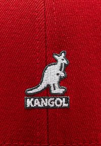 Cappello rosso con logo di canguro ricamato in bianco e testo "KANGOL" sottostante, che mostra un design in tessuto testurizzato e una forma semplice.