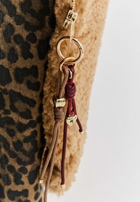 Zlatý klíčový přívěsek s hnědými a burgundskými šňůrkami a malými zlatými přívěsky ve tvaru srdce připojenými k huňaté hnědé látce a látce s leopardím vzorem.