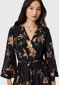 Vestido negro con estampado floral que presenta un escote en V profundo, mangas largas y una cintura elástica. La tela tiene una textura suave con patrones florales en beige y rosa.