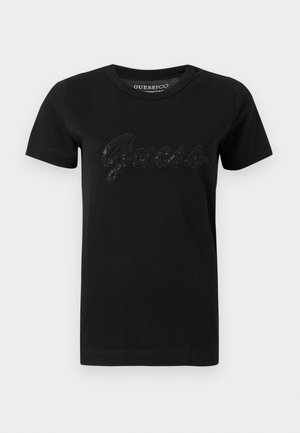 Melna kokvilnas T-krekls ar apaļu apkakli, īsām piedurknēm un teksturētu, spīdīgu "Guess" logotipu uz krūtīm.