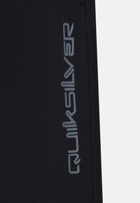 Juodos neopreno šortai su ryškiu pilku Quiksilver logotipu šone. Sklandus paviršius, prilipęs dizainas ir siūlėmis apipjaustyti kraštai.