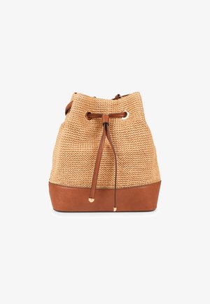 Woven tan straw bucket bag with a brown leather base. Drawstring closure with leather accents and metallic grommet details.