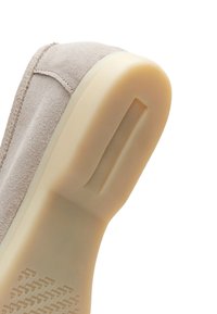 Chaussure en daim beige avec une semelle épaisse en caoutchouc clair, montrée en angle pour mettre en valeur le dessous texturé et les détails de couture.