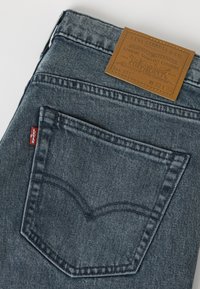 Poche arrière d'un jean Levi's gris foncé plié avec une étiquette rouge Levi's visible et une étiquette de marque en cuir marron indiquant la taille W32 L32.