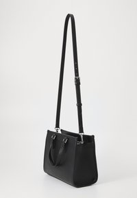Sac à main en cuir noir avec une forme structurée, deux poignées, une bandoulière réglable et des accents en métal argenté. La finition texturée complète le design.