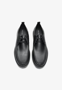 Zapatos de cuero negro con un acabado suave, con punta redonda, detalles de costura y un diseño simple de cordones. Suela de goma plana.