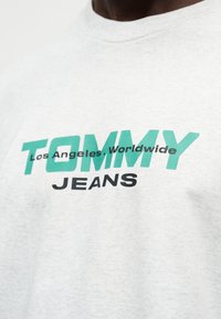 Γκρι βαμβακερό t-shirt με μεγάλο πράσινο και μαύρο λογότυπο "TOMMY JEANS" και κείμενο "Los Angeles, Worldwide" από κάτω. Μαλακή υφή.
