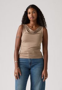 Tan ermeløs topp med drapert halslinje og samlet detalj på siden, paret med blå denimjeans som har en avslappet passform og lett tekstur.