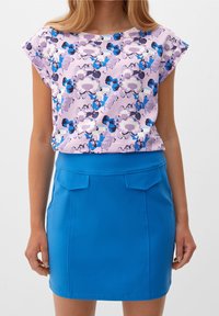Top floreale a maniche corte nei toni del viola e del blu abbinato a una gonna blu aderente con due tasche anteriori e una texture liscia.